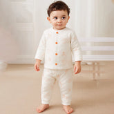 Toddler wearing cream-colored printed pajamas with orange buttons, standing indoors.