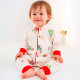 Smiling toddler wearing a romper with colorful prints and red cuffs, sitting indoors.