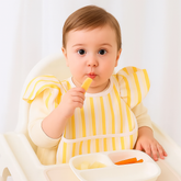 Baby wearing golden glow bib while eating in high chair.