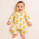 Smiling baby wearing a white jumpsuit decorated with bright yellow sunflower prints.