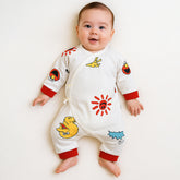 Smiling baby wearing a white jumpsuit with colorful cartoon prints and red cuffs.